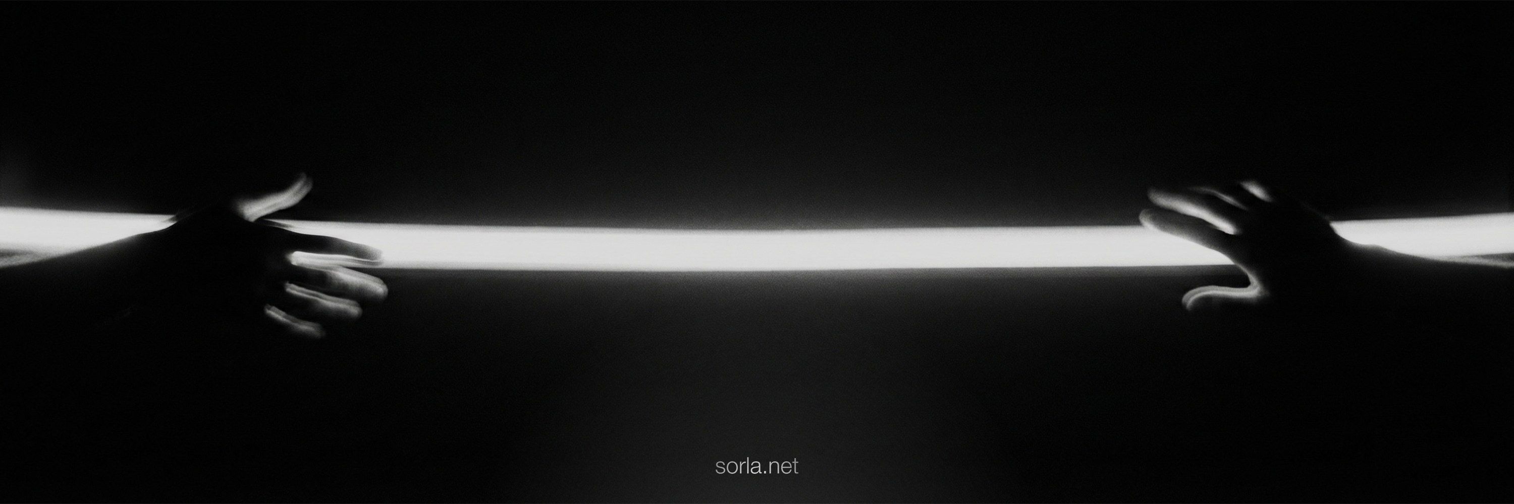 Two hands reaching toward a bar of white light in the dark