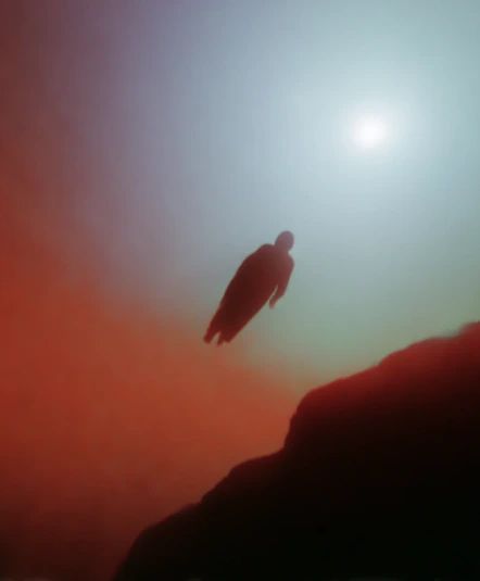 A dark figure floating in red and blue haze above a ridge