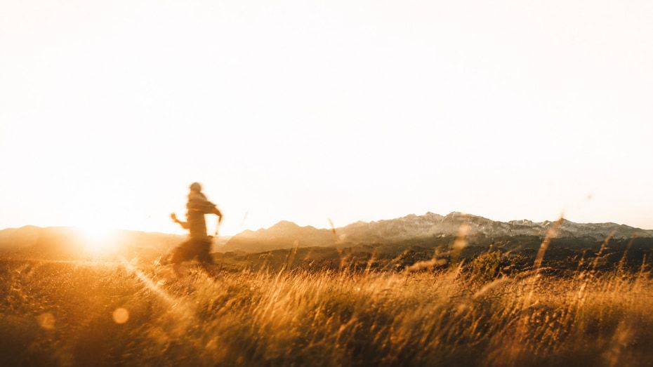 A runner crossing a golden field with mountains behind